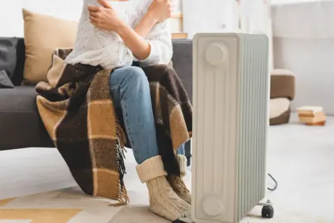 Zastanawiasz się, jaki grzejnik elektryczny do pokoju 25m2 będzie najlepszy? Ta osoba otulona kocem i w ciepłych skarpetach czeka na ciepło z nowego grzejnika.