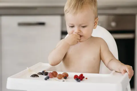 Chłopiec w krzesełku bada owoce, zastanawiając się, jakie warzywa dla 5 miesięcznego dziecka będą najlepsze na początek.