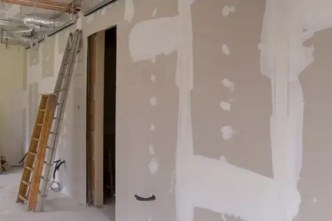Scianka dzialowa z plyty kartonowo gipsowej w trakcie prac. Widoczne drabiny, instalacje i otwór drzwiowy.