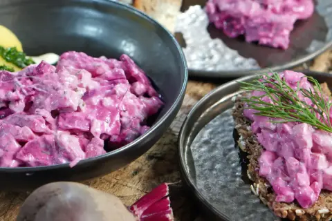 Omas roter Heringssalat, cremig und leuchtend pink, serviert mit Kartoffeln und auf Brot mit Dill.