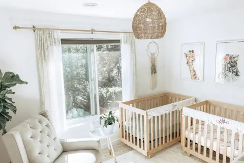 A serene twin m nursery with two wooden cribs, a plush armchair, and whimsical animal art.