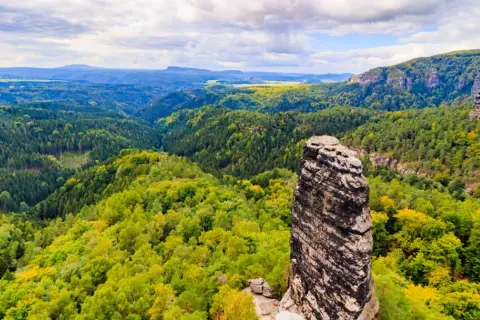 Piękne czeskie góry, gdzie jechać? Malowniczy krajobraz z dominującą skalną iglicą i bujnymi lasami.