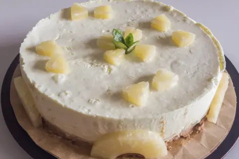 Pyszny sernik na zimno z ananasem, udekorowany kawałkami owoców i miętą. Idealny na letnie popołudnie.