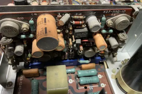 Wnętrze starego urządzenia elektronicznego z widocznymi kondensatorami, rezystorami i tranzystorami. Jeden z kondensatorów ma oznaczenie 220uF, a obok niego widać potencjalny problem z dc offset.