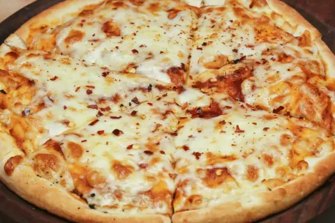 Pyszna pizza bez drożdży, obficie posypana serem i płatkami chili, pokrojona na kawałki.