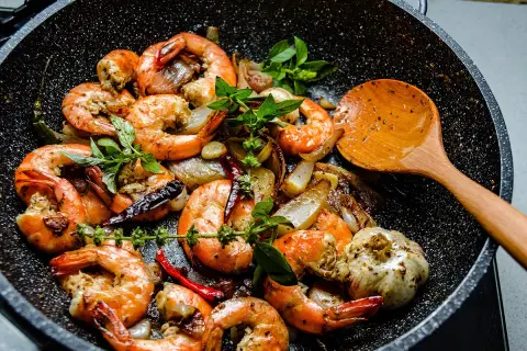 Gambas sautées à l'ail et au piment dans une poêle, prêtes pour le temps de cuisson. Une cuillère en bois est à côté.