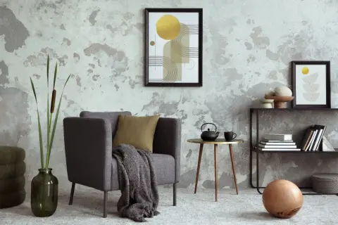 Salón moderno con pared texturizada que combina papel pintado y pintura. Sillón gris, mesa auxiliar dorada y arte abstracto.