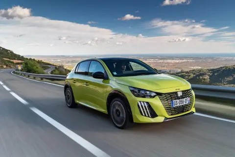 Jaskrawozielony Peugeot 208 na krętej drodze z widokiem na morze. Czy wady i zalety tego modelu skłonią Cię do zakupu?