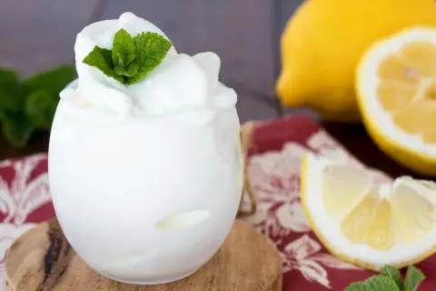 Sorbetto al limone fatto in casa, fresco e profumato, guarnito con menta. Accanto, limoni freschi e una tovaglietta rossa.