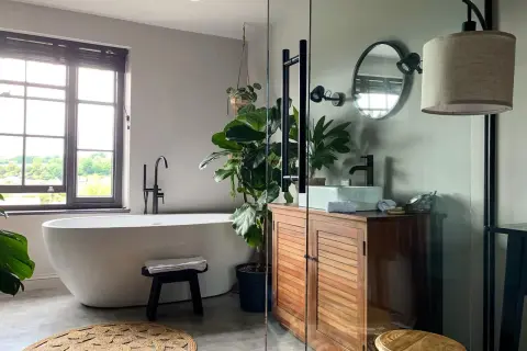 Une baignoire îlot, un meuble en bois et une plante luxuriante créent une ambiance de wet room apaisante.