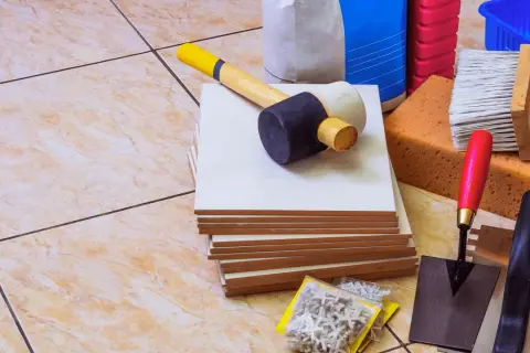 Outils pour coller du carrelage avec du ciment : carreaux, maillet, truelle, éponges, brosse, croisillons et sacs de ciment.