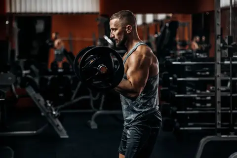 Siłacz ćwiczy biceps z ciężarem, czując napięcie w tricepsie.