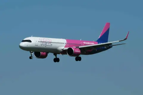 Samolot Wizz Air z różowym i niebieskim ogonem leci na tle błękitnego nieba.