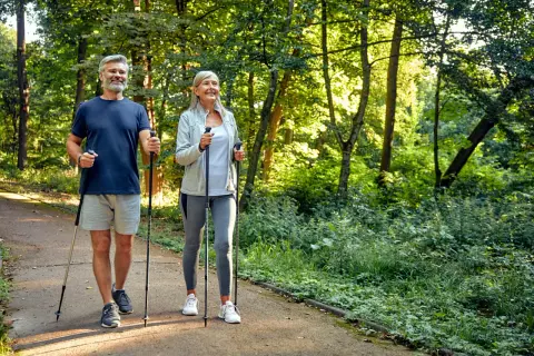 Älteres Paar genießt Nordic Walking im Wald. Eine gute Aktivität bei Bandscheibenvorfall zur Stärkung der Rückenmuskulatur.