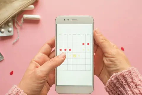 Dłoń trzyma smartfon z kalendarzem cyklu. Czy ginekolog może zbadać podczas okresu? Na ekranie zaznaczone dni miesiączki.