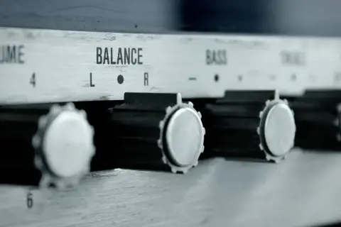 Nahaufnahme von Reglern eines Verstärkers: VOLUME, BALANCE, BASS. Ein Drehknopf für den gain regler ist gut sichtbar.