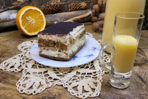 Sernik z pomarańczami i likierem pomarańczowym, obok połówka pomarańczy i kieliszek z likierem.