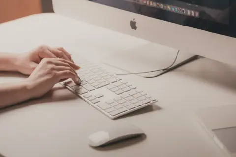 Mani che digitano su tastiera bianca, vicino a un mouse. Attenzione ai sintomi di tendinite da mouse per evitare dolori.