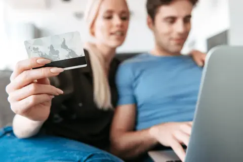 Kobieta trzyma kartę, mężczyzna pracuje na laptopie. Dane karty i PESEL to kluczowe informacje, jakie dane są potrzebne do wyłudzenia kredytu.
