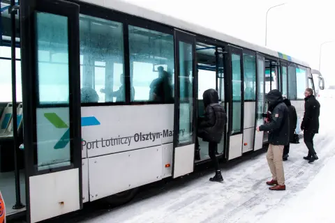 Szynobus z napisem "Port Lotniczy Olsztyn-Mazury" na tle śniegu, z pasażerami wsiadającymi.