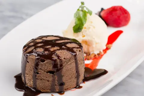 Un fondant au chocolat cœur coulant, servi avec une boule de glace à la vanille, une fraise et un coulis de fruits rouges.