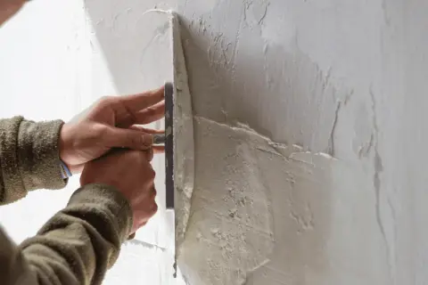 Mani esperte stendono il rasante su un muro, creando una superficie liscia e uniforme.