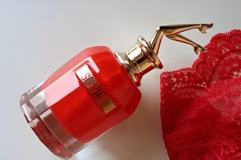 Czerwony flakon perfum Scandal EDP z złotymi nogami i koronkową bielizną. Zapach budzi skojarzenia z odwagą i zmysłowością.