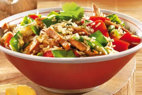 Schüssel mit Reis, Fleischstreifen, Paprika und Erbsen. Ein köstliches Gericht aus der Wok-Küche, garniert mit Koriander.