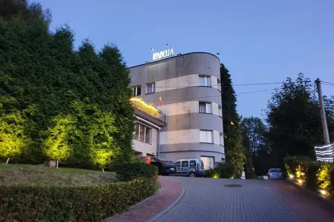 Elegancki hotel Izabella w Puławach, otoczony zielenią i oświetlony wieczorem. Zaprasza do odpoczynku.