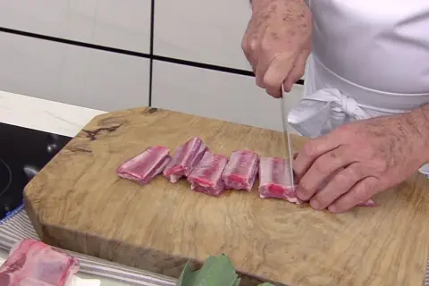 Chef corta costillas de cerdo en trozos para una deliciosa terrina de costilla.