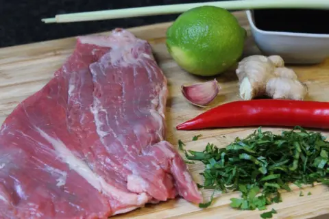 Rohes Rindersteak liegt bereit, um mit Limette, Ingwer, Chili, Knoblauch und Kräutern mariniert zu werden.