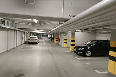 Wrocław główny parking cennik: podziemny parking z białym i czarnym Volkswagenem, białym BMW, rurami i klimatyzacją.