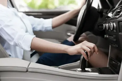 Dłoń kobiety na dźwigni zmiany biegów, przygotowująca do jazdy. Adaptacja skrzyni biegów w nowoczesnym samochodzie.
