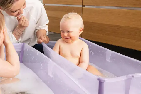 Glad bebis i badbalja, en mamma tittar på. Frågan "hur ofta bada bebis" kan besvaras med att det är mysigt att bada ofta!