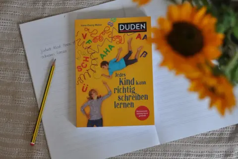 Ein Duden-Buch mit dem Titel "Jedes Kind kann richtig schreiben lernen" liegt auf einem Notizbuch. Ein Bleistift liegt daneben. Rechtschreib-training leicht gemacht.