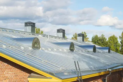 Nowoczesny dach z blachy na rabek, z kilkoma okrągłymi świetlikami i kominami.