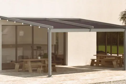 Pérgola moderna con techo oscuro, ideal para saber como cubrir un patio de la lluvia y disfrutar del exterior. Mesas de madera y zona ajardinada.