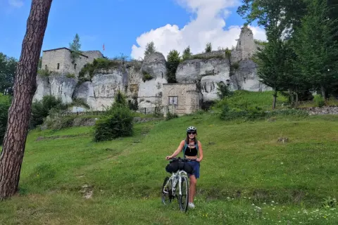 Kobieta z rowerem na tle ruin zamku na wapiennych skałach. Piękny dzień na trasie rowerowy szlak orlich gniazd.