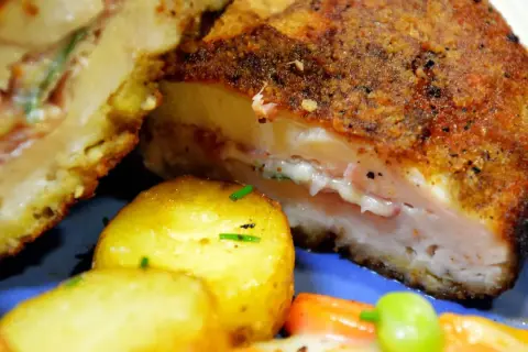 Kotlet po szwajcarsku, złocisty i chrupiący, z rozpływającym się serem i szynką w środku, podany z ziemniaczkami.