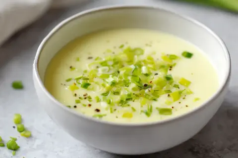 Un bol de fondue de poireaux crémeuse, garnie de poireaux frais hachés et de poivre noir.