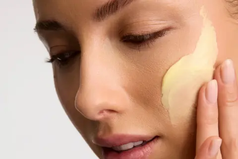 Application d'une crème riche en céramides pour une peau éclatante. Les doigts doux étalent la texture onctueuse.