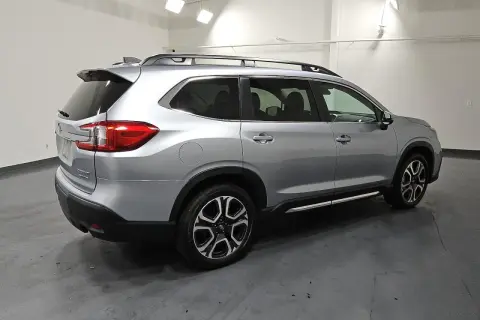 Srebrny Subaru Ascent z relingami dachowymi i przyciemnianymi szybami stoi na ciemnej podłodze.
