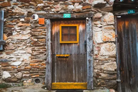 Puerta de madera rústica en una pared de piedra en la serrada de la fuente. Números 20, 28 y 18 adornan la entrada.