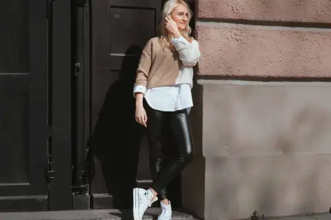 Styling-Tipp: So kannst du lederleggings kombinieren. Eine Frau mit blonden Haaren trägt sie mit einem weißen Hemd und einem zweifarbigen Pullover.
