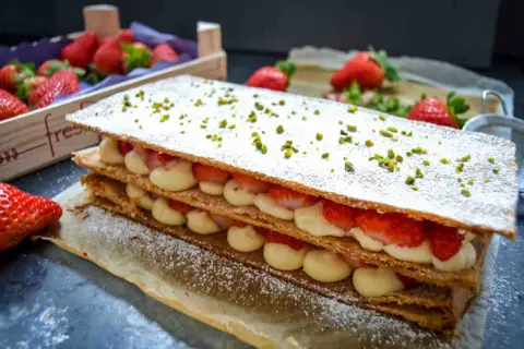 Ein köstliches Mille-feuille mit frischen Erdbeeren und Sahne, bestreut mit Puderzucker und Pistazien.