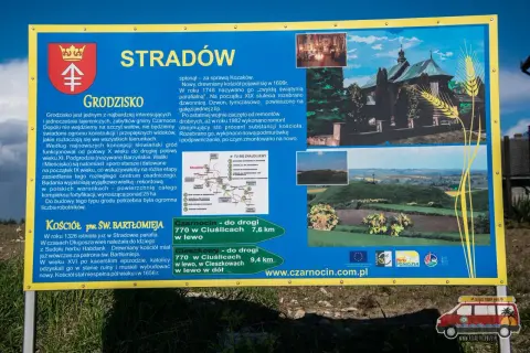 Tablica informacyjna o grodzisku Stradów, jego historii i kościele pw. św. Bartłomieja. Widok na krajobraz z wałami grodziska.