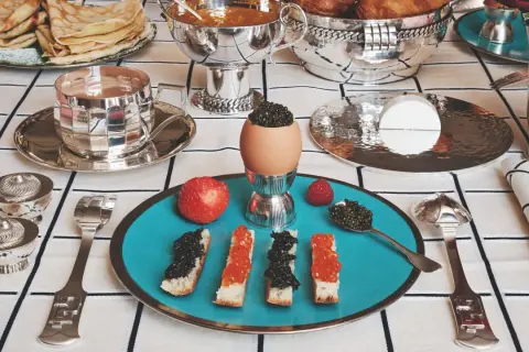 Un festin de caviar, toasts, œufs et fruits sur une table dressée avec une nappe au motif damassé.