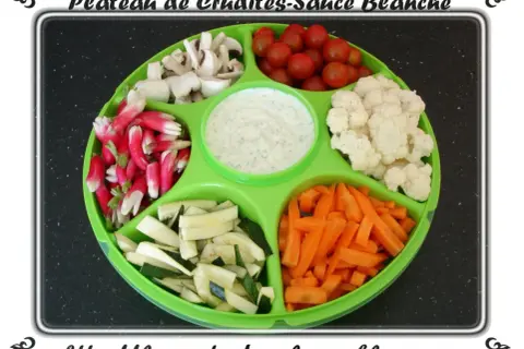 Plateau de crudités coloré : radis, champignons, tomates cerises, chou-fleur, courgettes et carottes, avec une sauce blanche au centre.