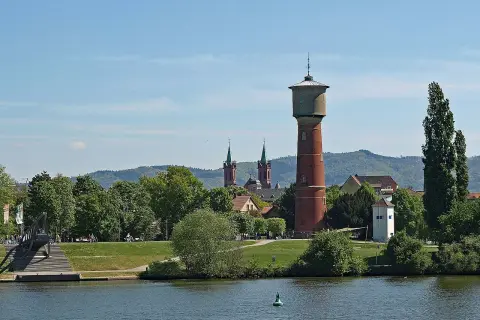 Wasserturm und Kirchtürme über grünen Bäumen, die die ladenburg altstadt säumen, mit Fluss im Vordergrund.