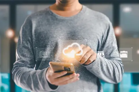 Osoba trzymająca smartfon z ikonami chmury, książki i folderów.